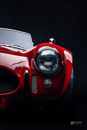 Détail avant d’une voiture ac cobra de collection rouge avec phare rond, photographie fine art automobile sur fond sombre.