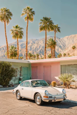 Porsche 911 classique blanche stationnée devant une maison Mid-Century Modern à Palm Springs avec des palmiers et les montagnes californiennes en arrière-plan.