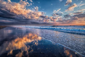 Coucher de soleil sur la Côte Sauvage de Quiberon avec vagues de l’Atlantique et nuages colorés se reflétant sur le sable mouillé.